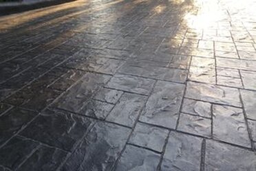 Dark grey colored stamped concrete surface with stone pattern and high gloss finish